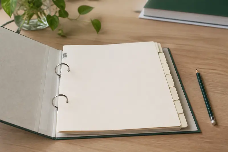 Un classeur d’archives ouvert sur un bureau en bois clair, intercalaires pâles vierges et un crayon