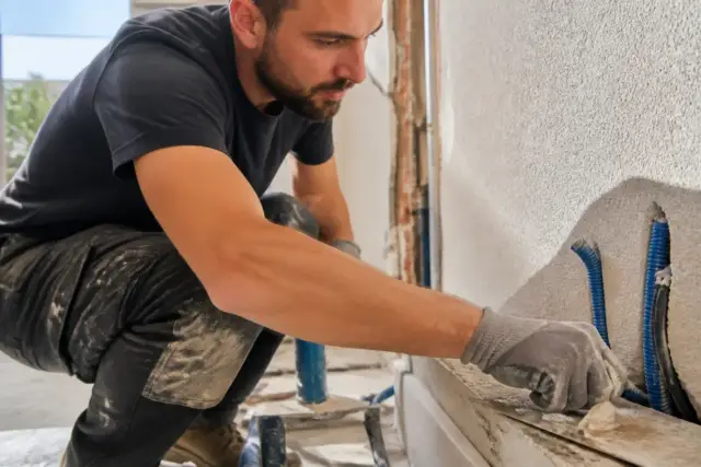 Un homme rénove un mur en plâtre pour construisonbusiness.fr dédié aux auto-entrepreneurs