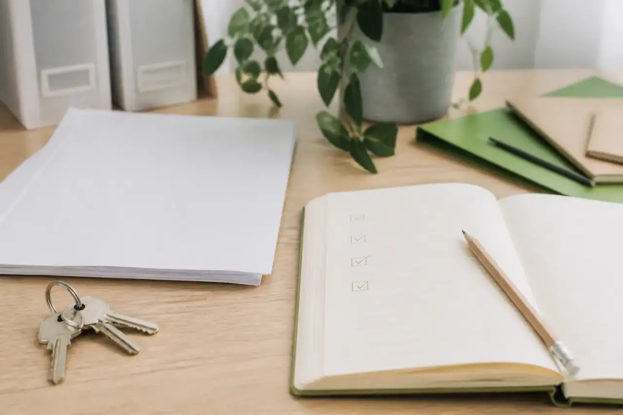 Clés, acte de vente et stylo posés sur un comptoir en bois, carnet ouvert avec une liste de formalités cochées au crayon