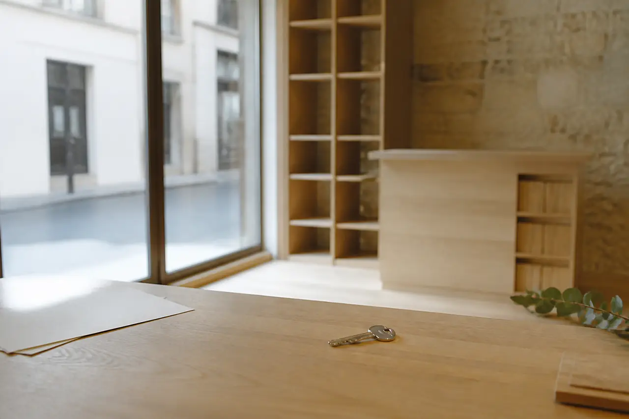 Une clé posée sur un comptoir en bois clair devant la vitrine vide d’une petite boutique, lumière douce