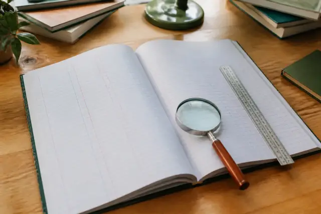 Gros registre ouvert sur une table, lignes datées écrites au stylo, une loupe et une règle posées sur la page