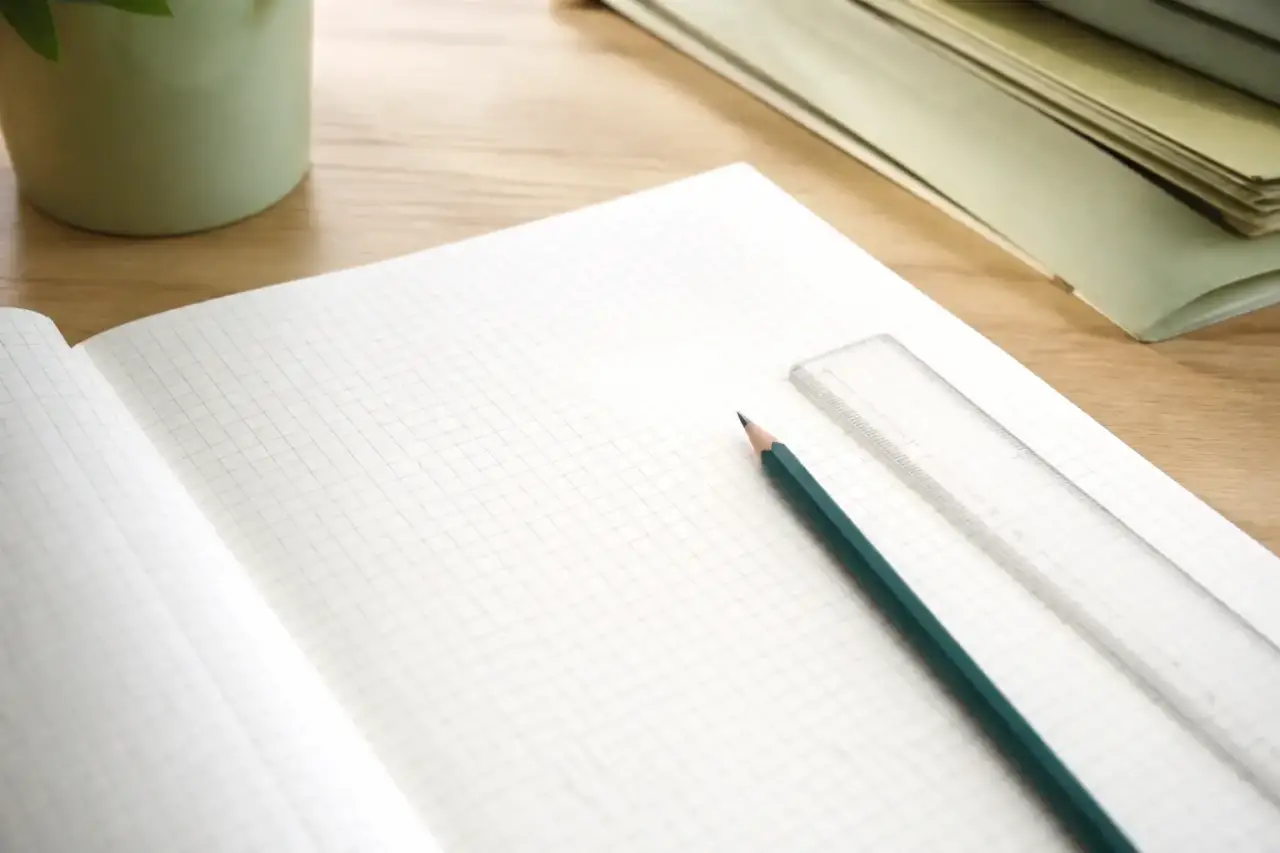 Carnet ouvert sur une page quadrillée où sont alignés des numéros de compte à trois chiffres, un crayon et une règle plate