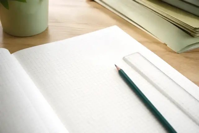 Carnet ouvert sur une page quadrillée où sont alignés des numéros de compte à trois chiffres, un crayon et une règle plate