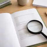 Carnet ouvert sur une facture annotée au crayon, une loupe posée sur la ligne de TVA, lumière douce sur un bureau en bois