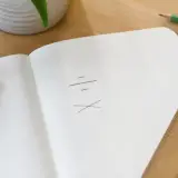 Page de carnet avec une fraction manuscrite, un prix toutes taxes comprises barré d’un trait de crayon, une règle plate